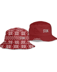 The image shows both sides of the reversible bucket hat. The one red side  featuring the Stōk logo in white lettering on the front. The other shows the alternate reversible side of the red bucket hat with a festive, knitted pattern design featuring white snowflakes and geometric shapes throughout. The Stōk logo is displayed in white on the front of the hat, maintaining a clean and simple contrast against the intricate design.