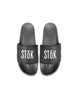 Black rubber slides with the white Stōk logo written across the strap of both.