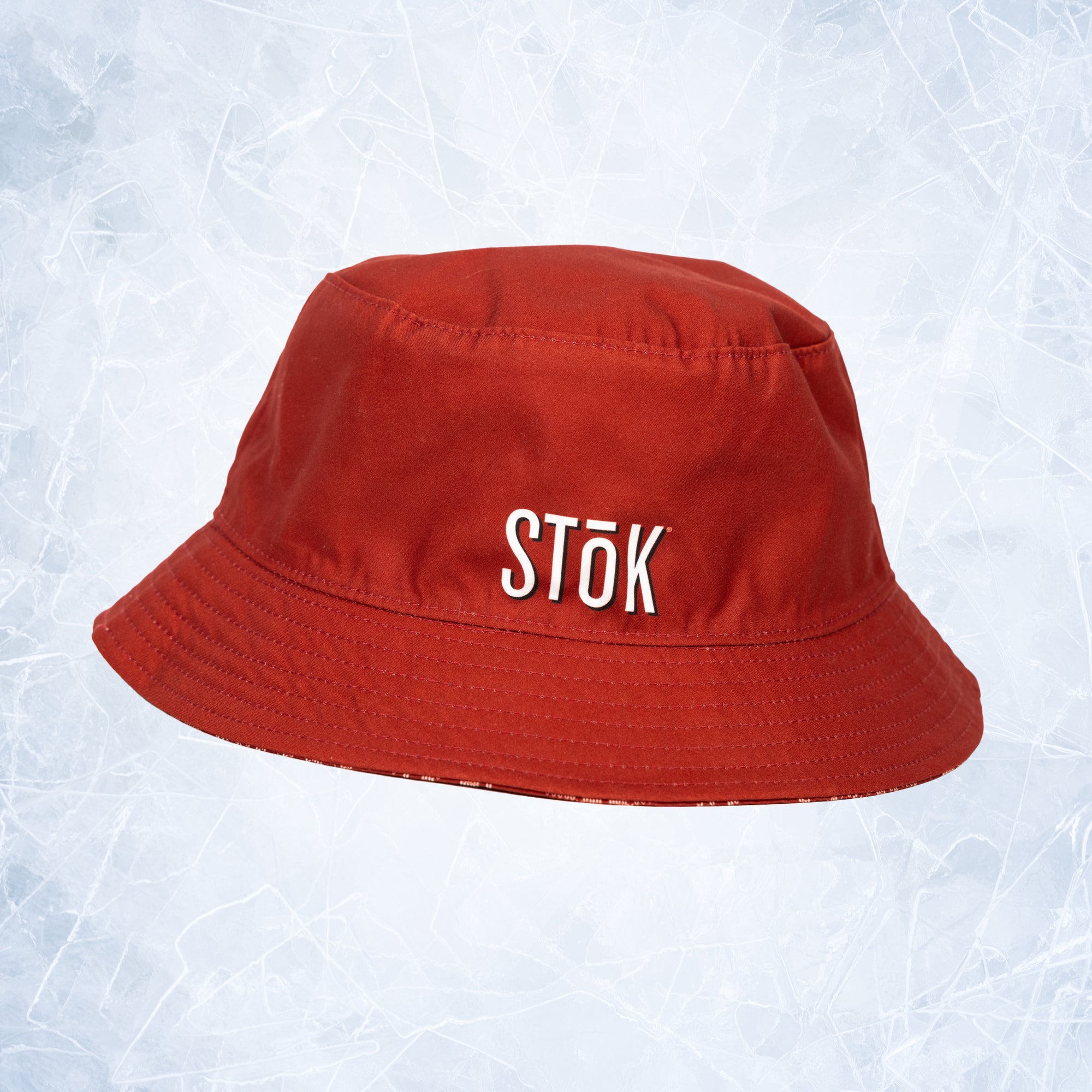 A red bucket hat featuring the Stōk logo in white lettering on the front. The image hints at the other side of the bucket hat resembling a festive, winter theme.