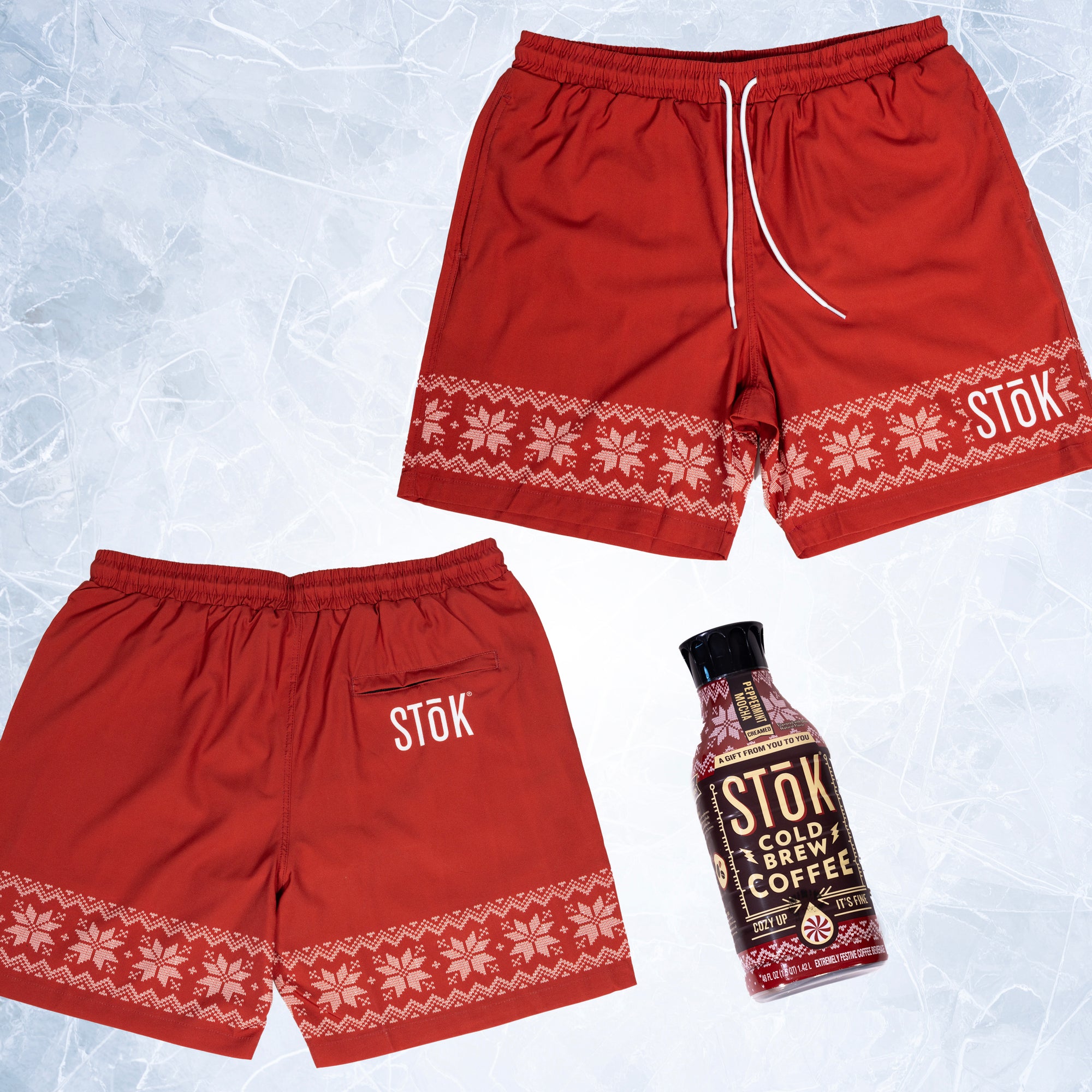 The front and back of red swim trunks with a strip of knitted pattern design featuring white snowflakes and geometric shapes across the bottom of the legs. The Stōk logo is displayed in white on the left leg strip of pattern, maintaining a clean and simple contrast against the intricate design. There is a white shoelace like tie closure on the front of the waistband next to a Stōk cold brew