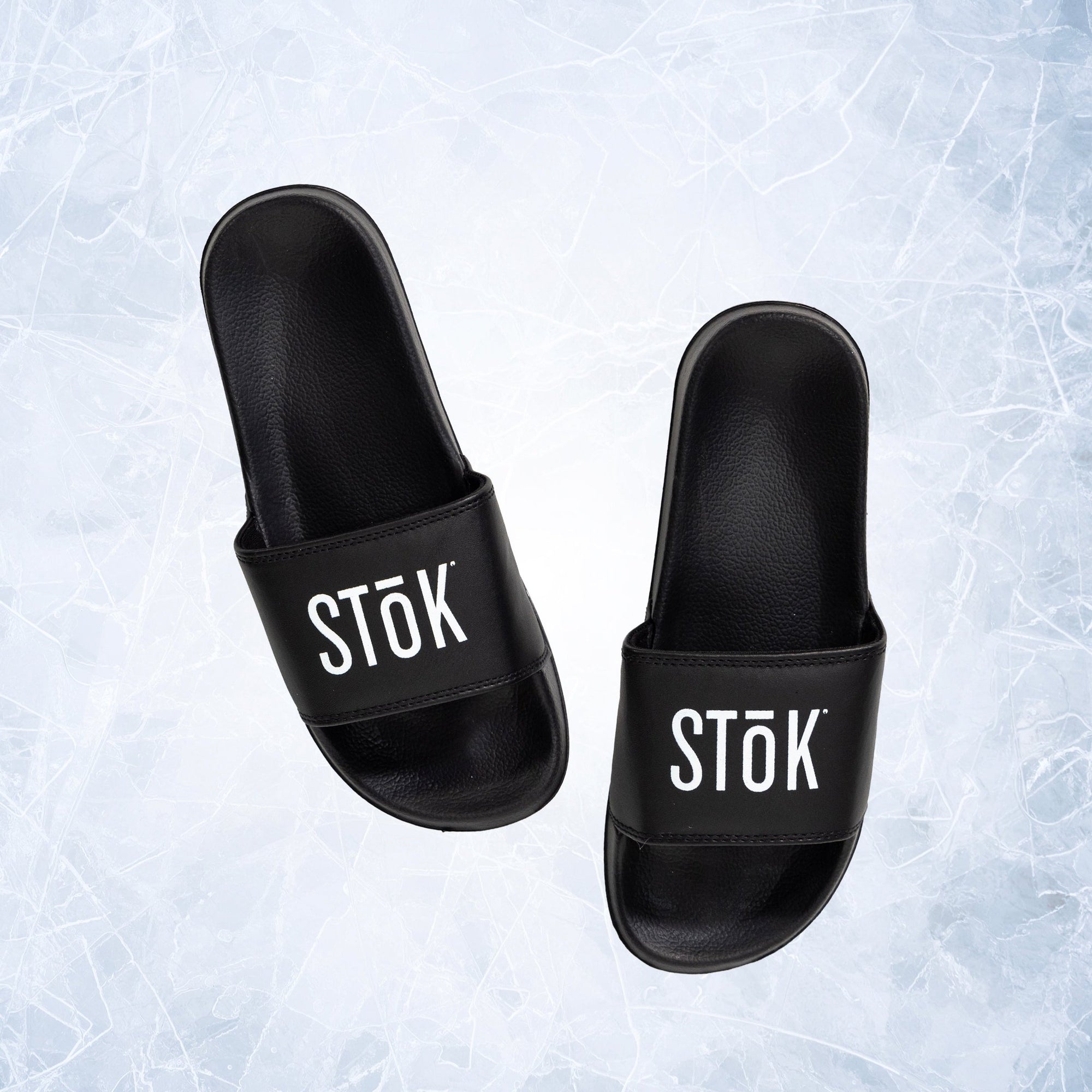 Black rubber slides with the white Stōk logo written across the strap of both.