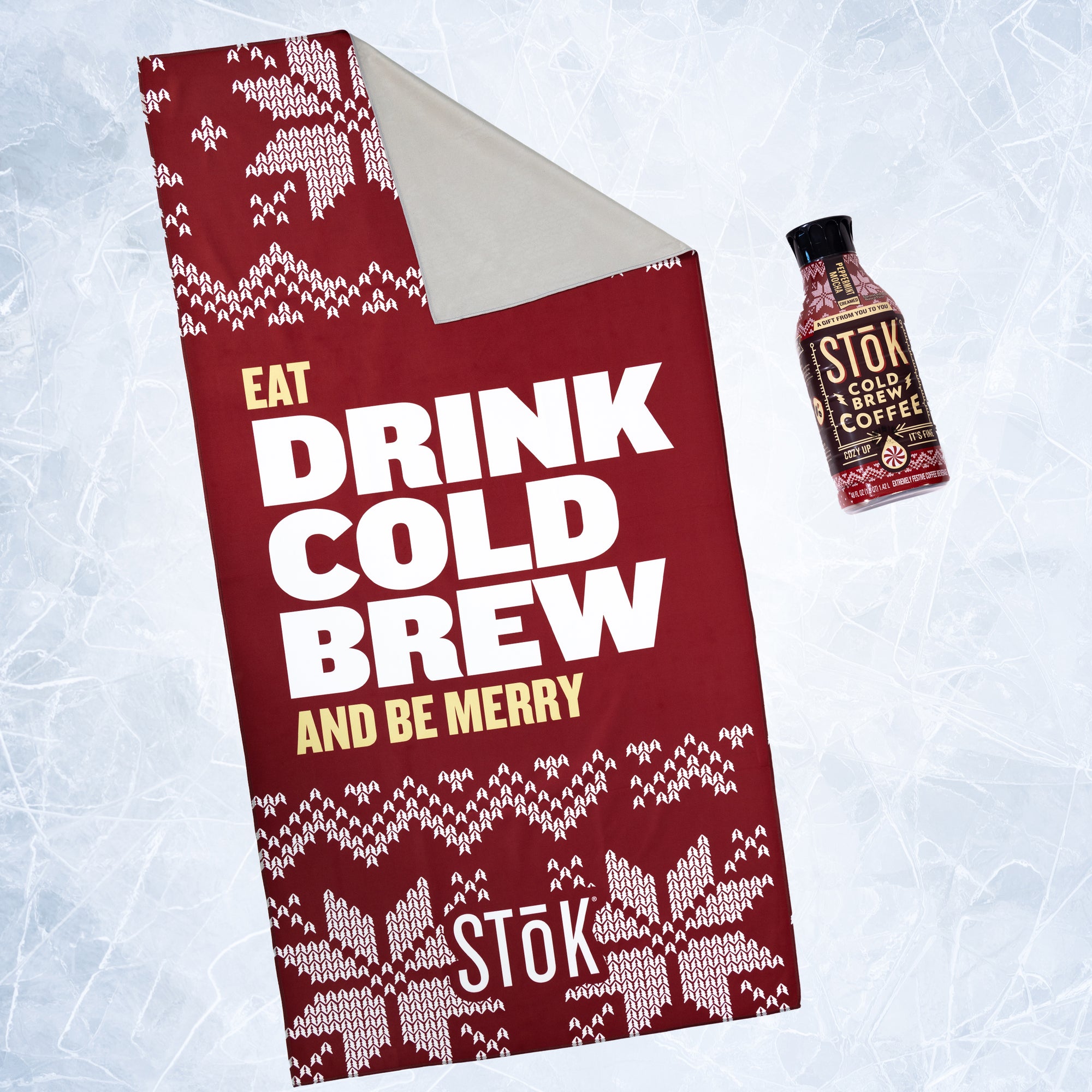 A red towel for Stōk cold brew coffee featuring a holiday-themed design. The sign has a red background with white knitted patterns resembling snowflakes and festive decorations. The large text in the center reads ‘EAT DRINK COLD BREW AND BE MERRY,’ with ‘Stōk’ logo displayed at the bottom next to a Stōk Cold Brew